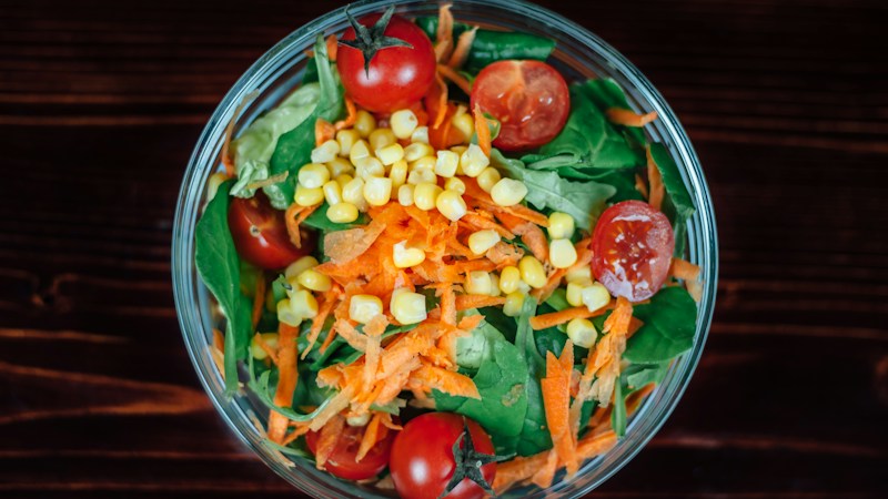 A bowl of vegetables with spinach, carrots, corn and tomatoes